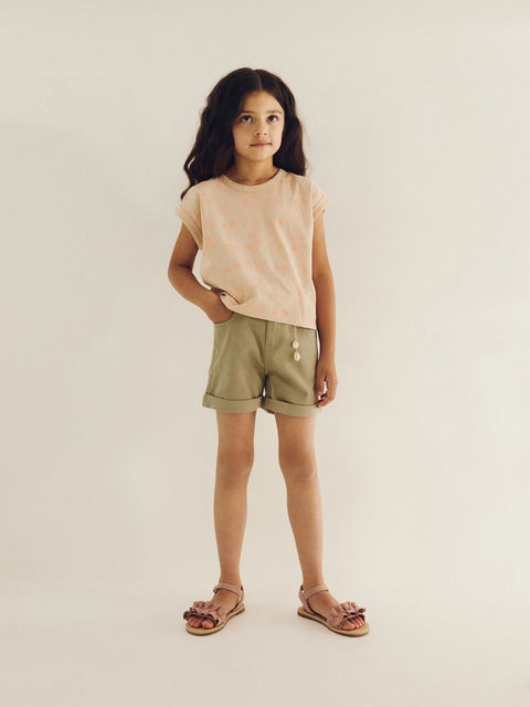 Young girl wearing a beige top and shorts on a plain background