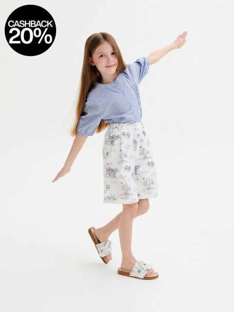 Young girl wearing a blue shirt and floral shorts on a white background