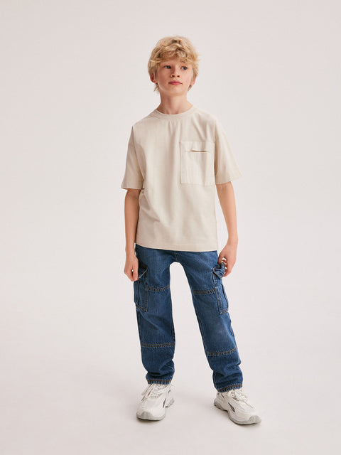 Young person wearing a beige t-shirt and blue jeans on a white background