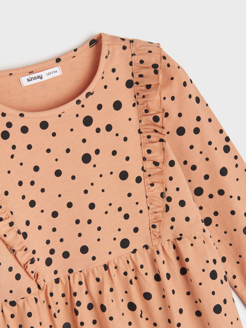 Close-up of a peach-colored dress with black polka dots on a white background