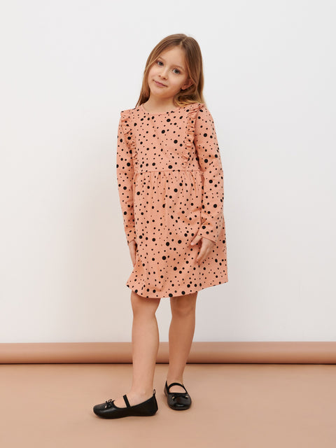 Young girl wearing a pink dress with black polka dots against a plain background
