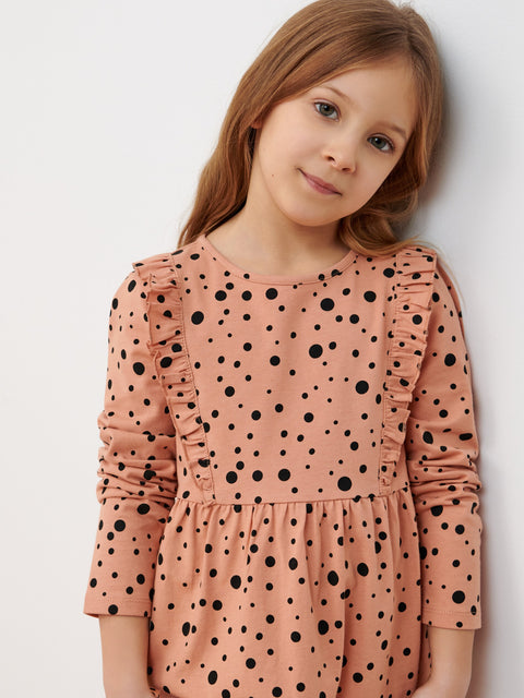 Young girl wearing a pink dress with black polka dots against a white background