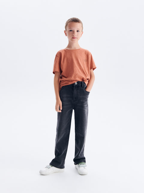 Child wearing a brown shirt and black pants on a white background