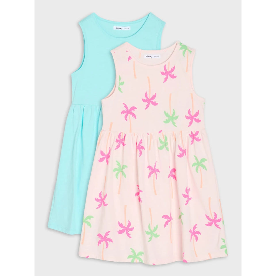 Two sleeveless children's dresses by Baby Phat, shown flat-laid on a light gray background. The front dress is pale pink with a pink and green palm tree print, and the back dress is light aqua blue.