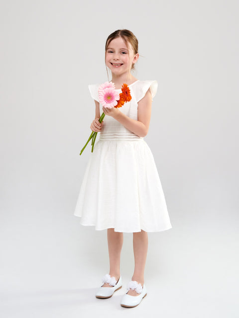 Young girl in a white dress holding flowers against a plain background