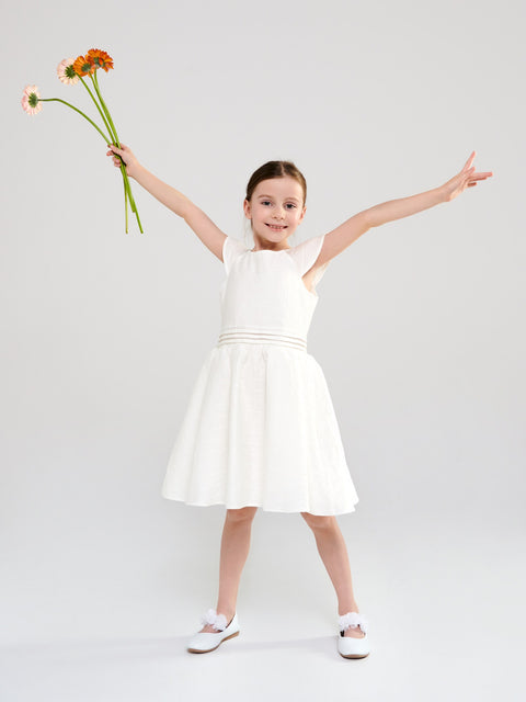 Young girl in a white dress holding flowers against a plain background