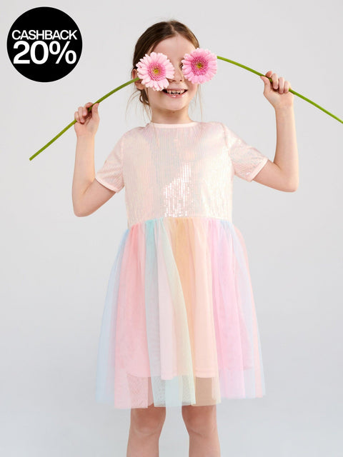 Young girl wearing a pastel dress holding pink flowers over her eyes against a white background