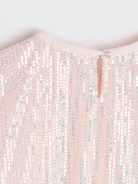 Close-up of a sequined garment with a soft pink background