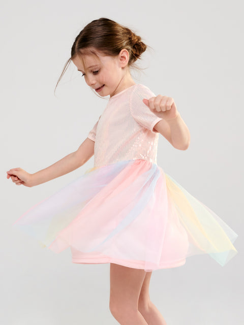Young girl wearing a pastel dress with a rainbow skirt on a light gray background