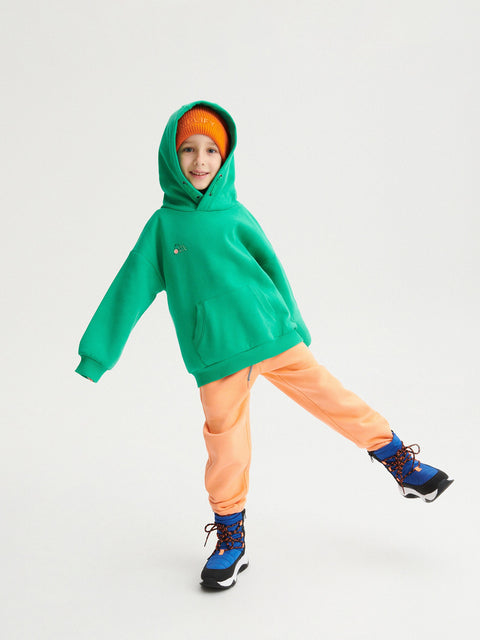 Child wearing a green hoodie and colorful outfit on a light gray background