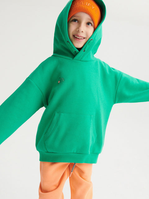 Child wearing a green hoodie and orange pants on a white background