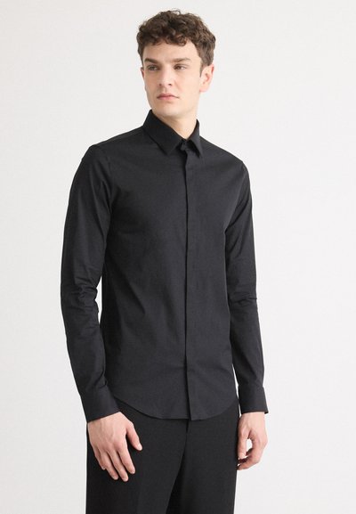 Man wearing a black dress shirt and pants on a white background