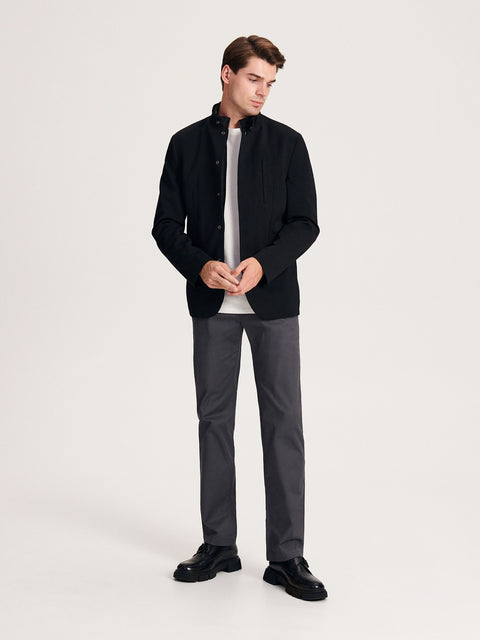 Man wearing a black jacket, gray shirt, gray pants, and black shoes on a white background
