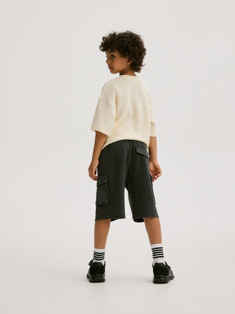 Child wearing a white shirt and black cargo shorts on a white background