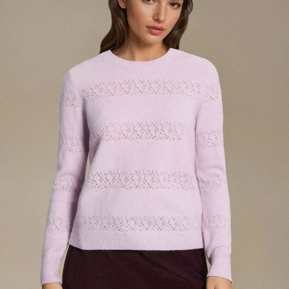 A woman wearing a light pink knit sweater with horizontal lace-like pattern bands, paired with a dark brown skirt, against a solid beige background.