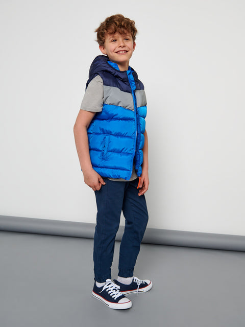 Child wearing a blue puffer vest over a gray shirt with navy pants on a plain background