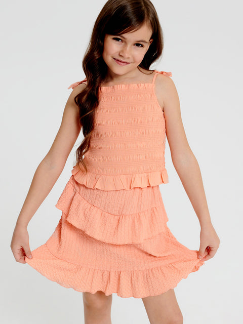 Young girl wearing a peach-colored dress with ruffled layers on a white background