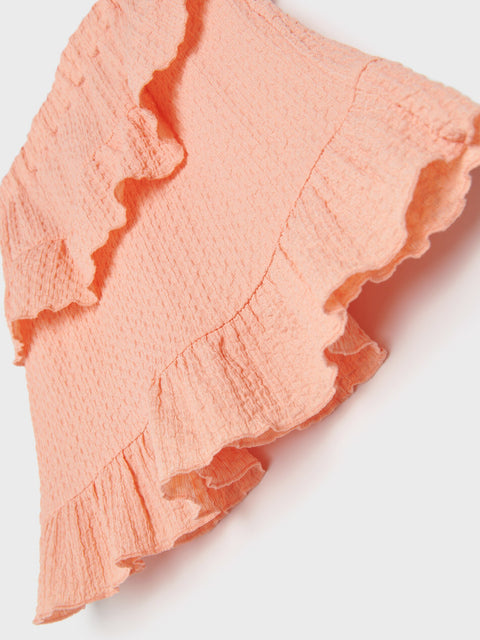 Close-up of a textured peach-colored fabric with ruffled edges on a white background