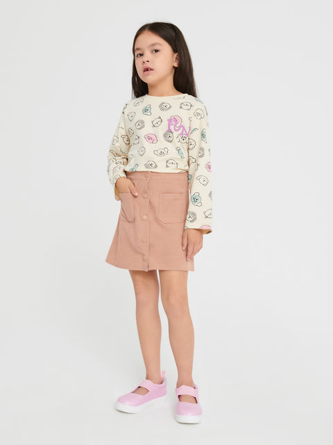Young girl wearing a patterned top and beige skirt on a white background