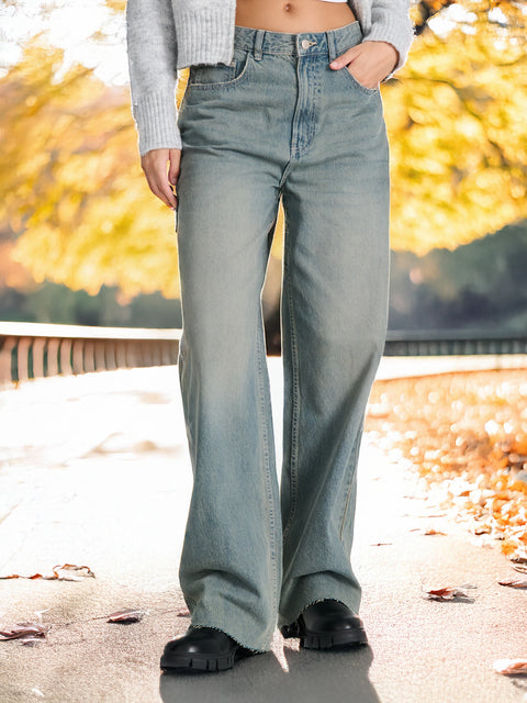 Person wearing light blue jeans and a gray sweater with a blurred autumn background