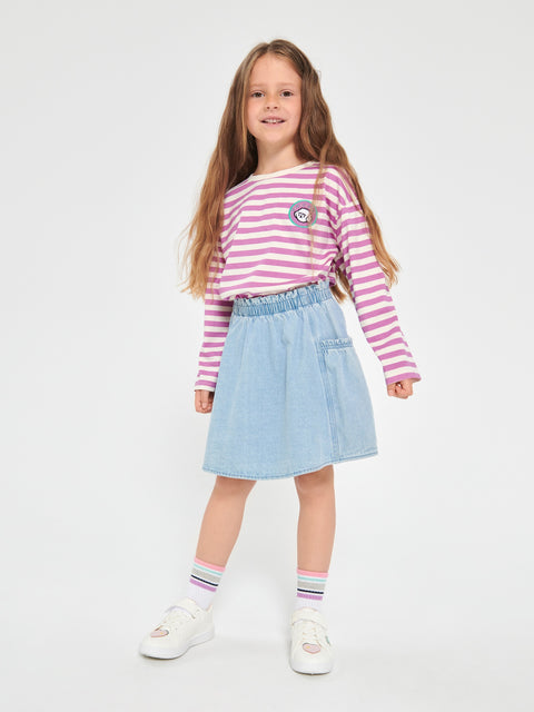 Young girl wearing a pink and white striped shirt with a denim skirt on a white background