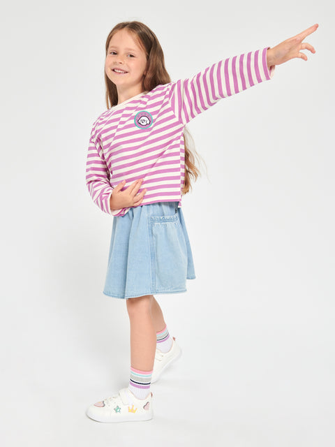Young girl wearing a pink and white striped shirt with a denim skirt on a white background