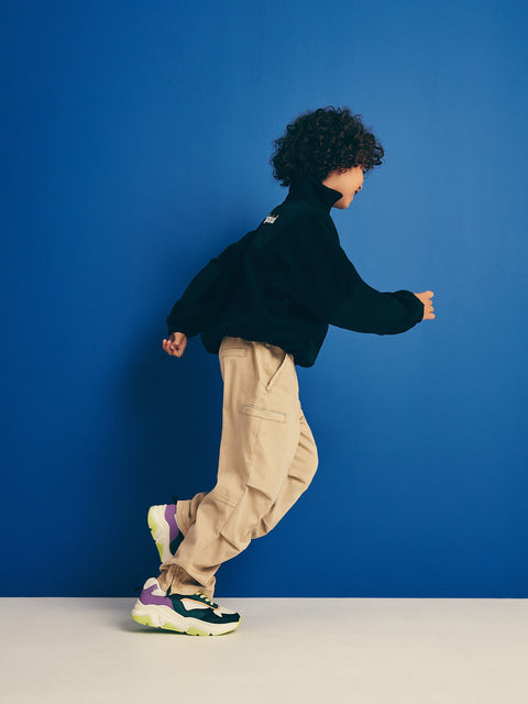 Person wearing a black jacket, beige pants, and colorful sneakers against a blue background