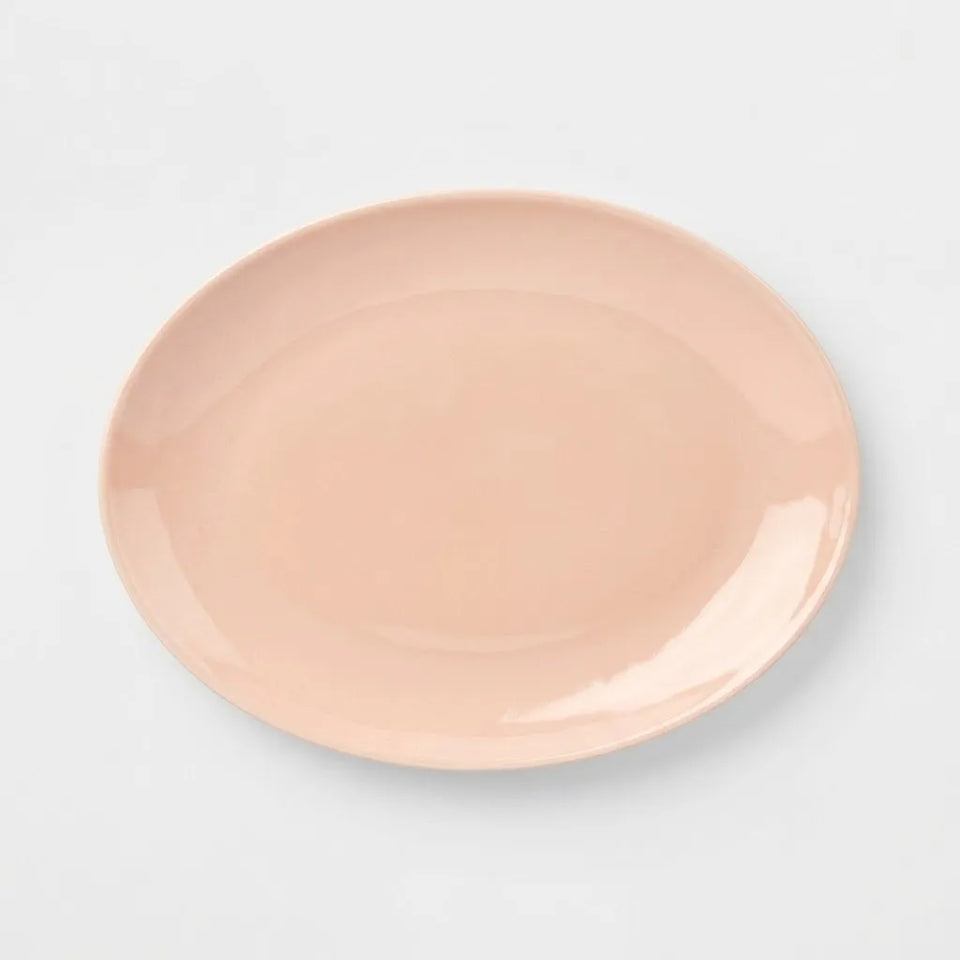 A minimalist, oval-shaped ceramic serving platter in a soft peach-pink color, shown from a top-down perspective on a clean white background.