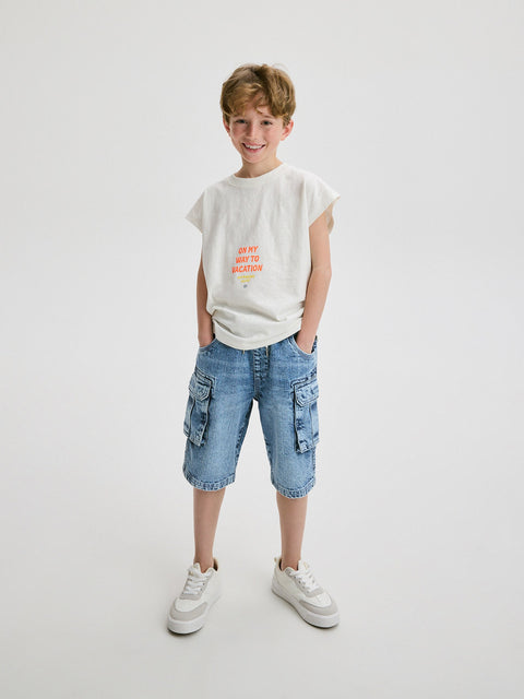 Young boy wearing a white t-shirt with text and blue cargo shorts on a light gray background