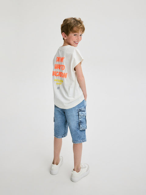 Child wearing a white t-shirt with colorful text and blue shorts on a light gray background