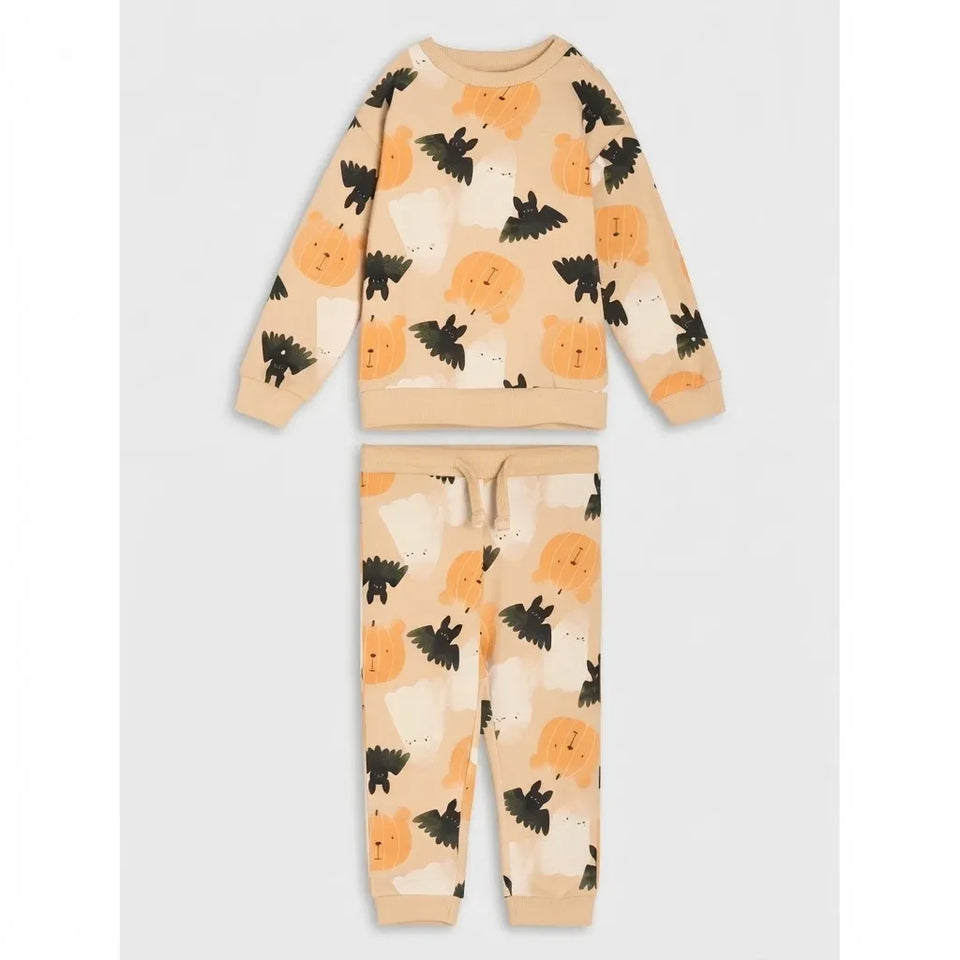 A two-piece children's pajama set featuring a long-sleeve sweatshirt and matching pants in a warm beige color, decorated with a playful pattern of orange pumpkins, black bats, and light brown teddy bears on a white background.