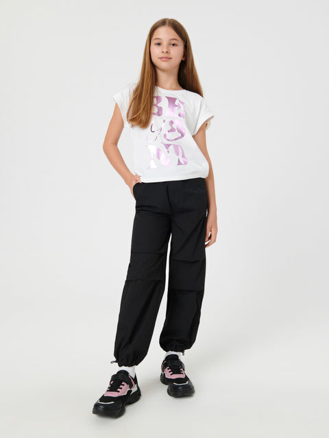 Young girl wearing a white t-shirt with a graphic design and black pants on a white background
