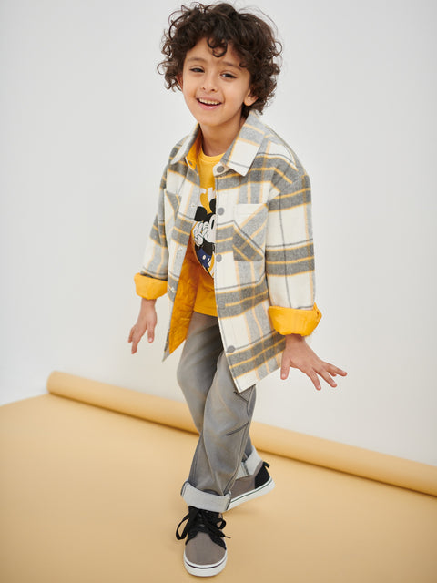 Child wearing a plaid shirt with yellow accents and gray pants on a white background
