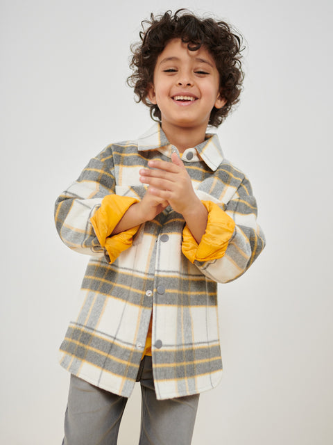 Child wearing a plaid shirt with yellow cuffs and interior, standing against a plain background