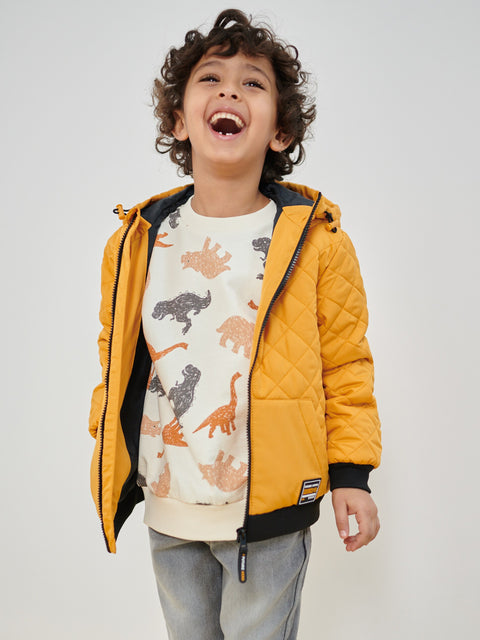 Child wearing a yellow quilted jacket over a dinosaur-patterned shirt on a plain background