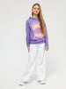 Young girl wearing a purple hoodie with a colorful graphic and white pants on a white background