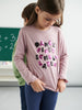 Young girl wearing a pink shirt with sequin text in a classroom setting