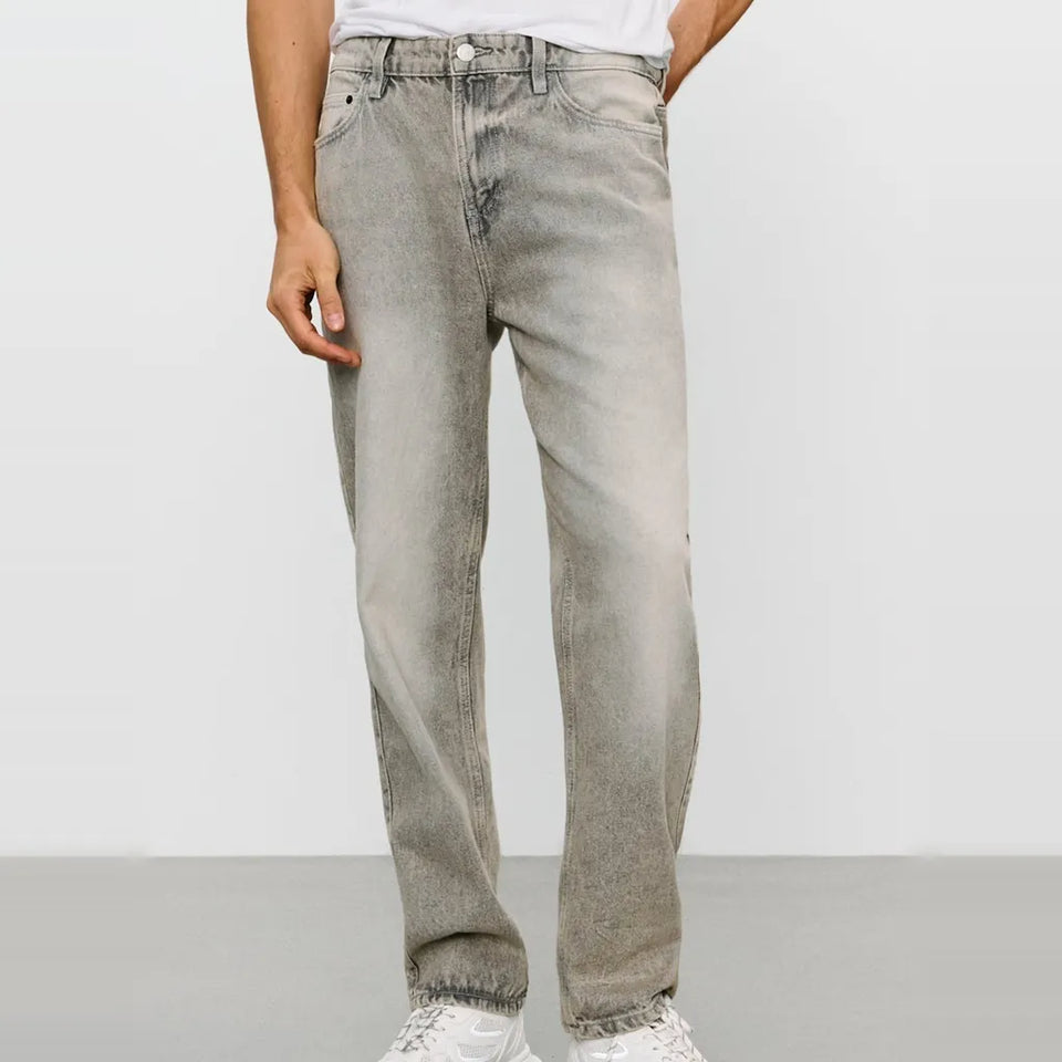 A person wearing light gray washed denim jeans with a faded finish, paired with a white t-shirt and white sneakers, shown from the waist down against a plain light gray studio background.