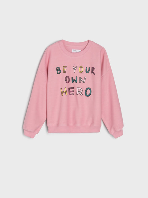 Pink sweatshirt with 'Be Your Own Hero' text on a light gray background