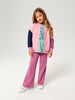Young girl wearing a colorful outfit with a pink jacket and purple pants on a white background