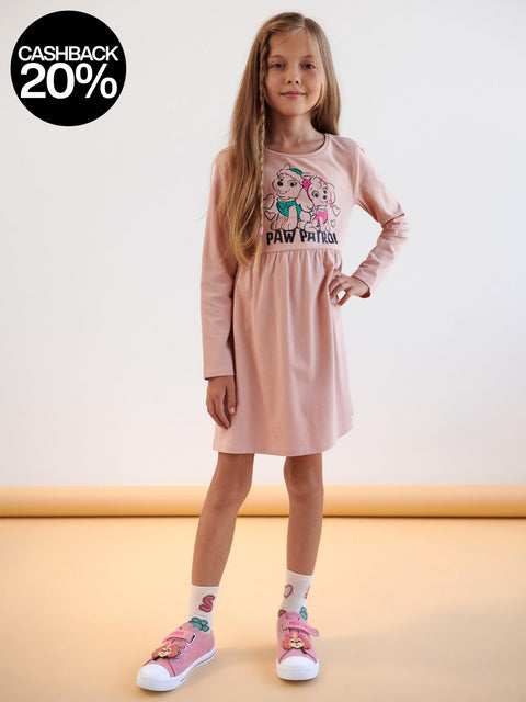Young girl wearing a pink 'Paw Patrol' dress with matching shoes on a beige background