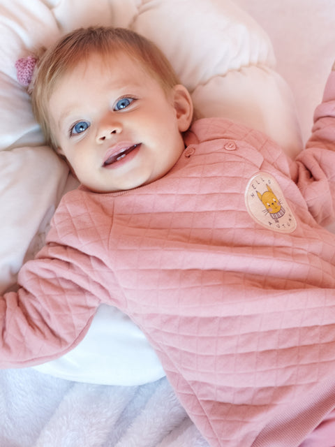 Baby in a pink outfit lying on a soft surface