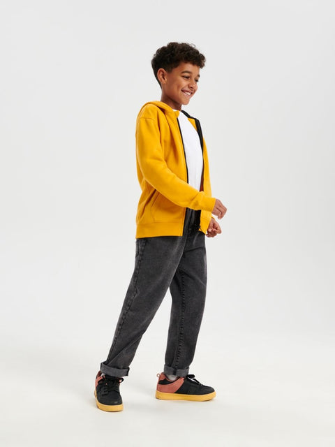 Person wearing a yellow cardigan, black shirt, gray pants, and black shoes on a white background