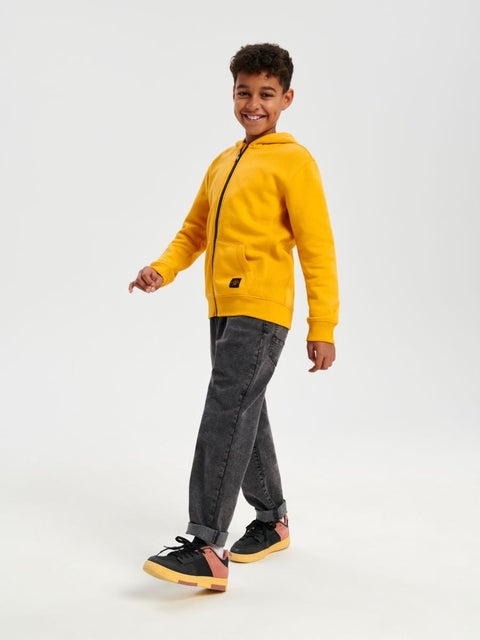 Child wearing a yellow hoodie and gray pants on a white background