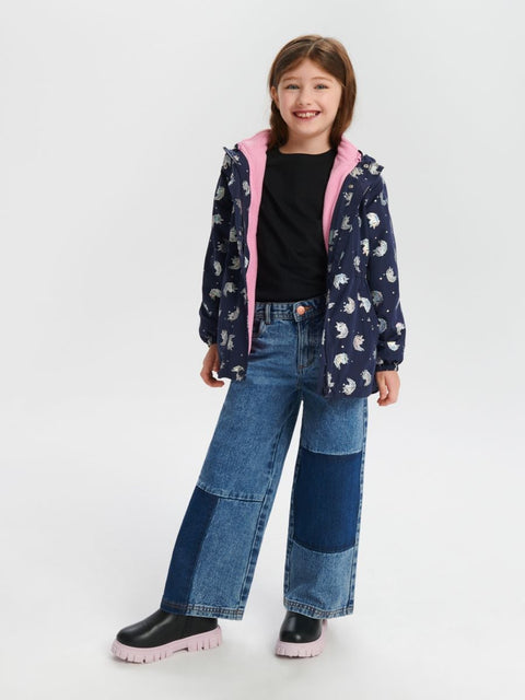 Child wearing a navy jacket with pink lining and patchwork jeans on a white background
