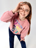 Young girl wearing a pink sweatshirt with colorful graphics on a white background