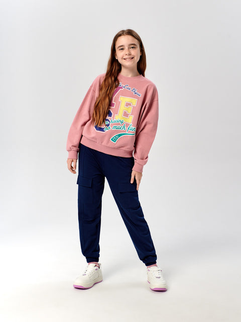 Girl wearing a pink sweatshirt with colorful graphics and navy pants on a white background
