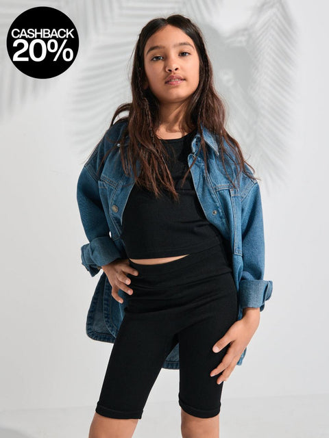 Person wearing a denim jacket over a black top and shorts on a white background