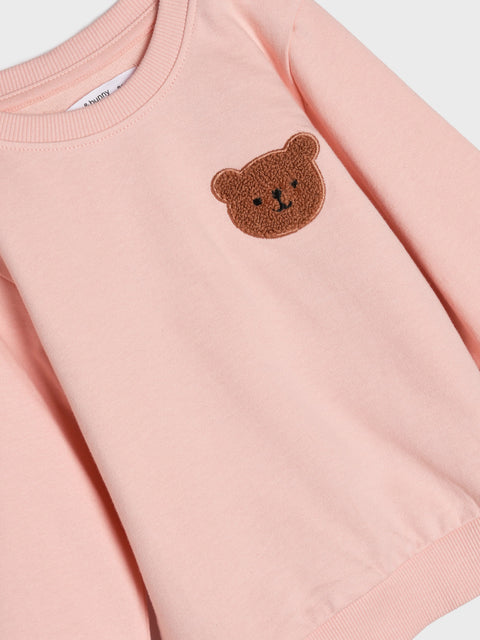 Pink sweatshirt with a brown bear patch on a white background