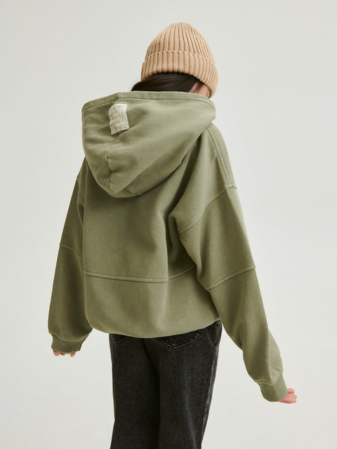 Person wearing a green hoodie and beige beanie on a plain background